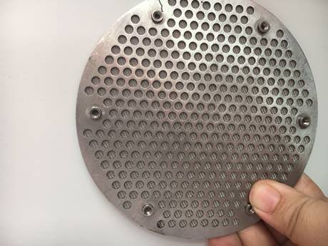 A hand is holding a round shape perforated metal sintered filter disc.
